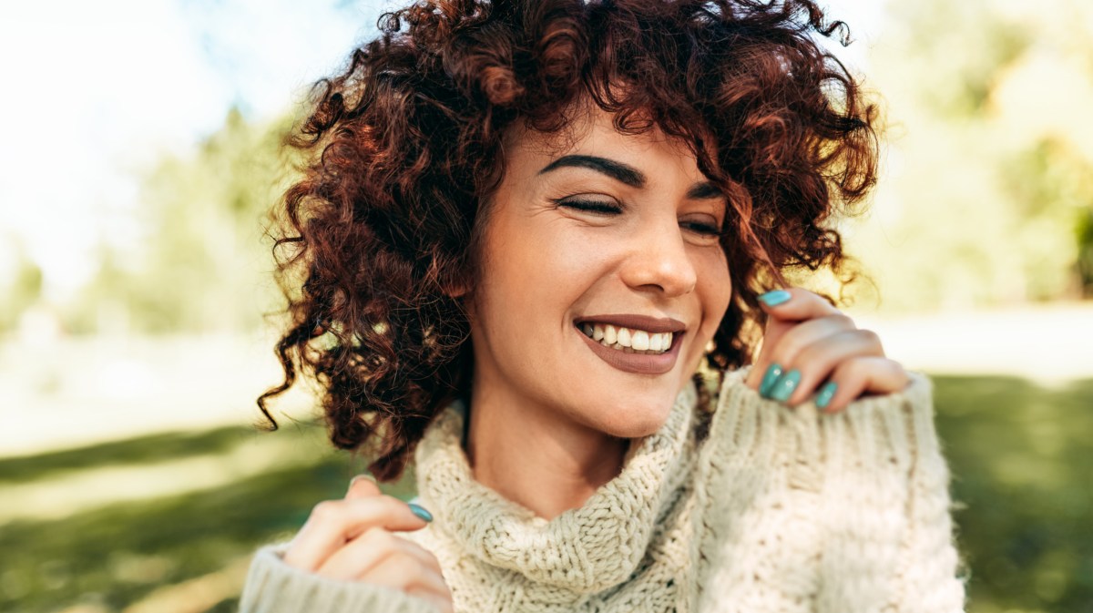 Frau mit Locken und blauem Nagellack, die sich lächelnd zur Seite dreht