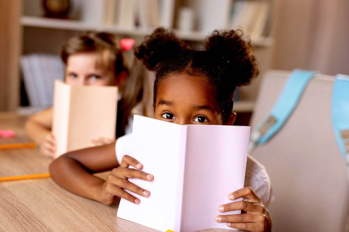 Zwei Mädchen verstecken sich hinter ihren Büchern, die sie in der Bibliothek lesen.