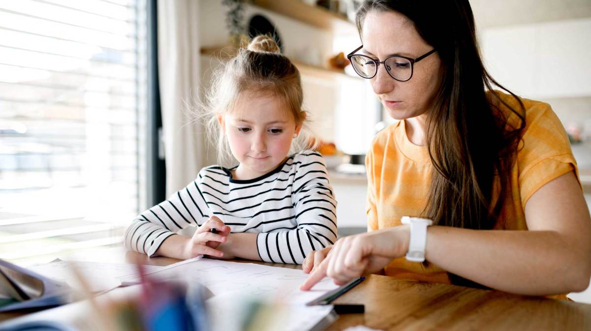 Mutter und Tochter sitzen an einem Tisch und schauen sich Schulmaterialien an.