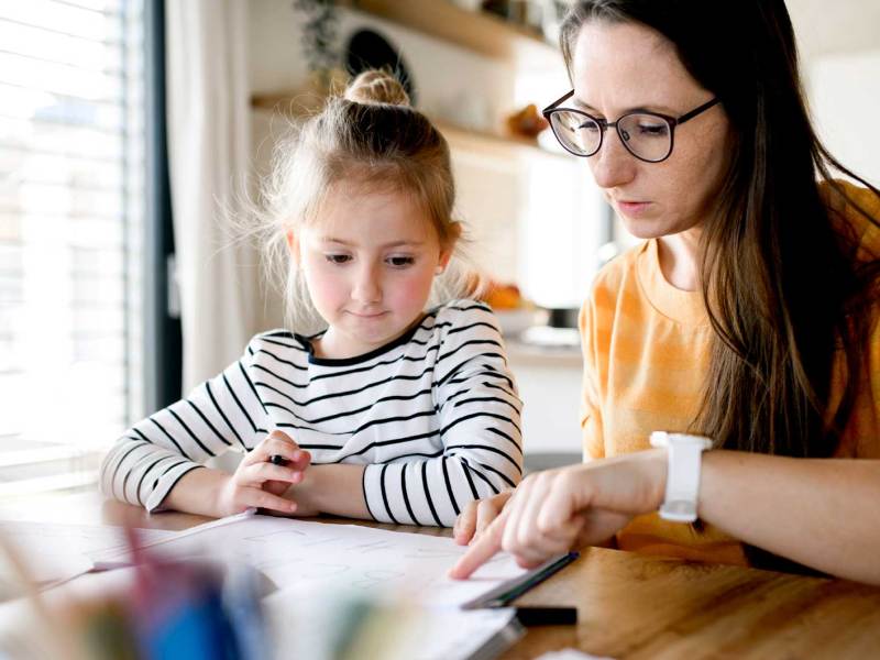 Mutter und Tochter sitzen an einem Tisch und schauen sich Schulmaterialien an.