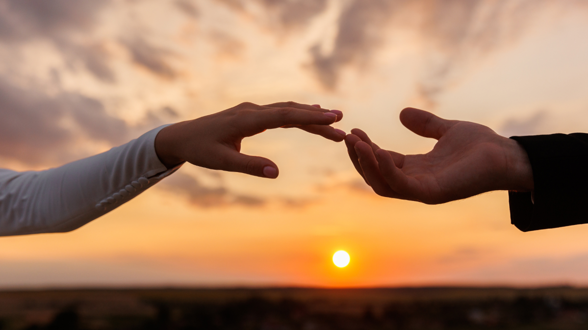 Zwei Hände vor einem Sonnenuntergang, die sich berühren