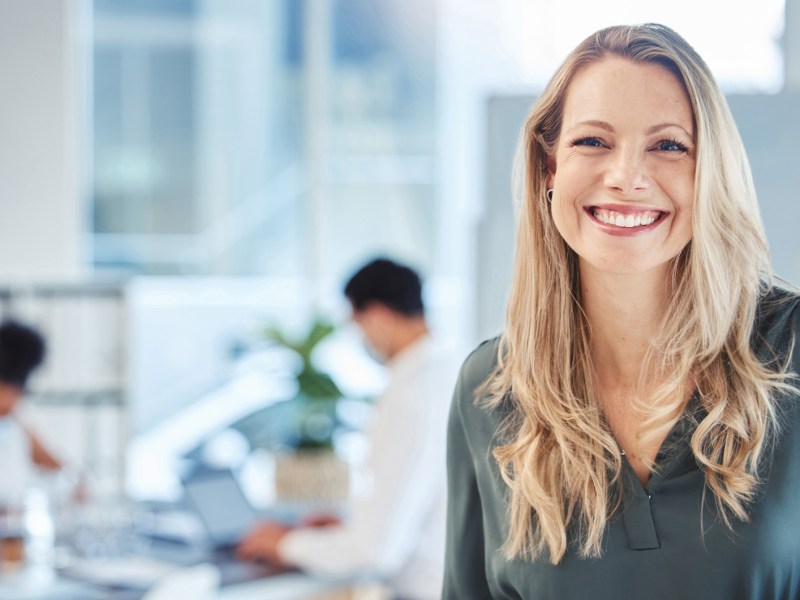 Blonde Frau auf der Arbeit lächelt in die Kamera.