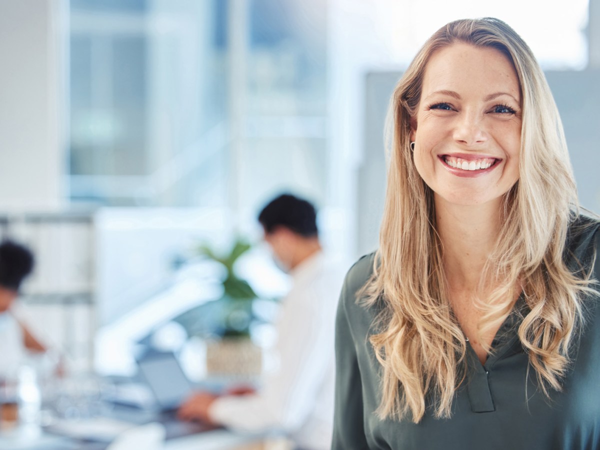 Blonde Frau auf der Arbeit lächelt in die Kamera.