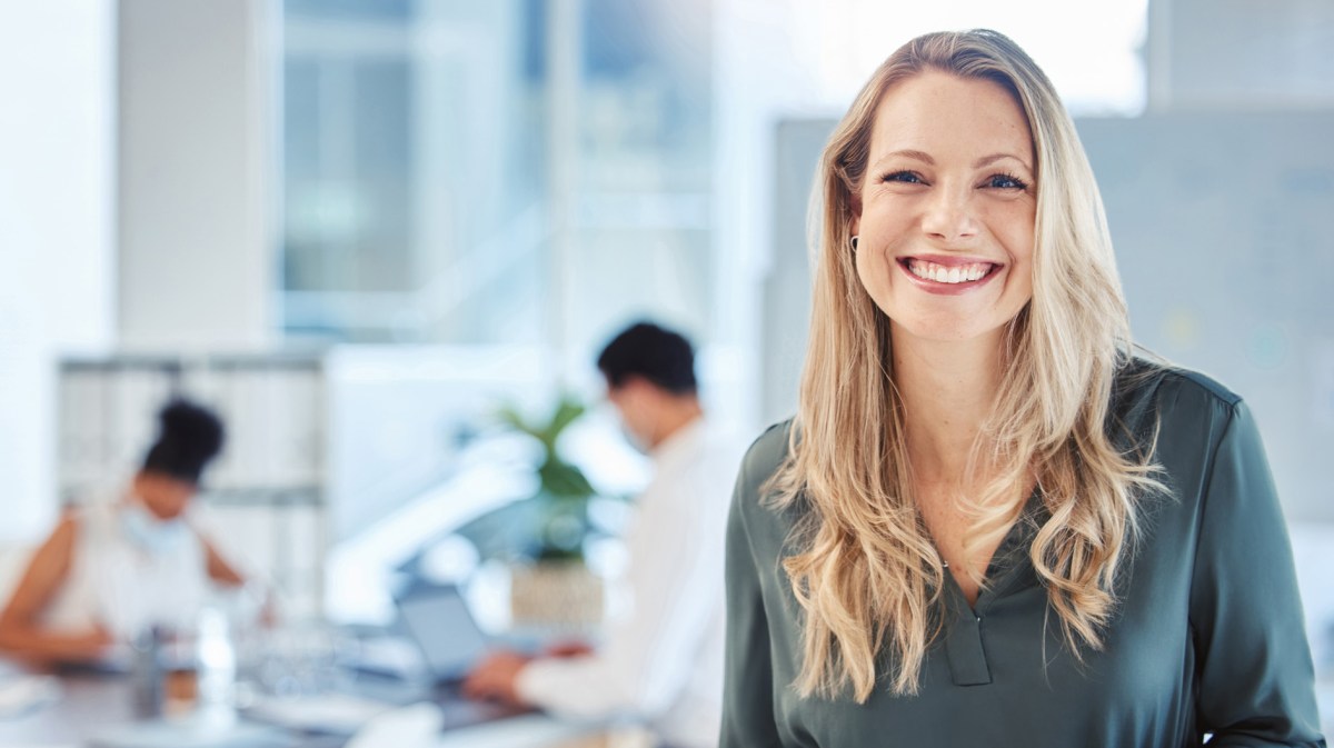 Blonde Frau auf der Arbeit lächelt in die Kamera.