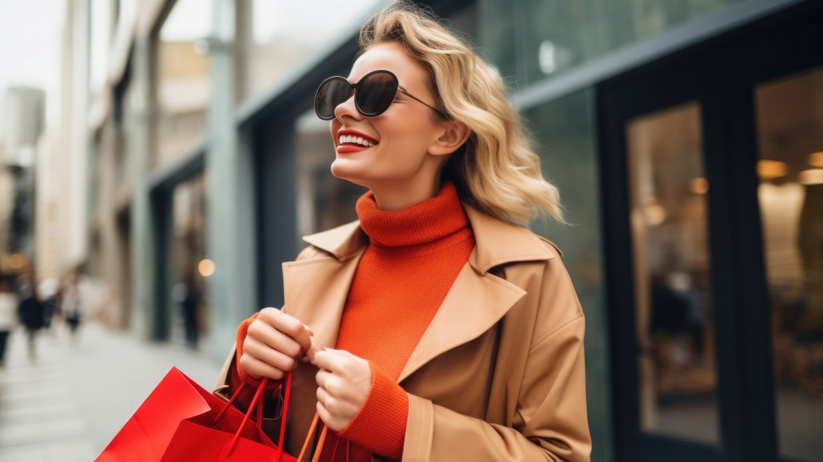 Frau mit Shopping-Tasche in der Hand und Sonnenbrille auf, die durch die Stadt geht und lächelt