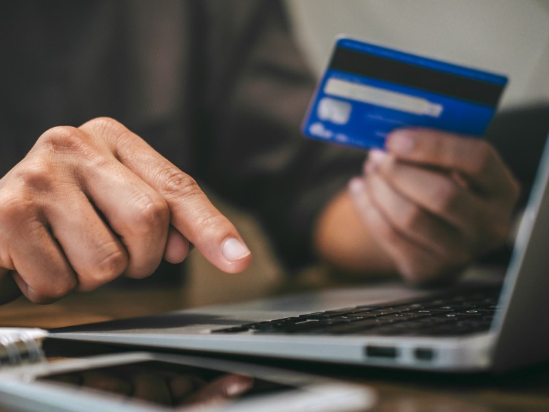 Frau hält Bankkarte in der Hand und tippt auf dem Laptop.