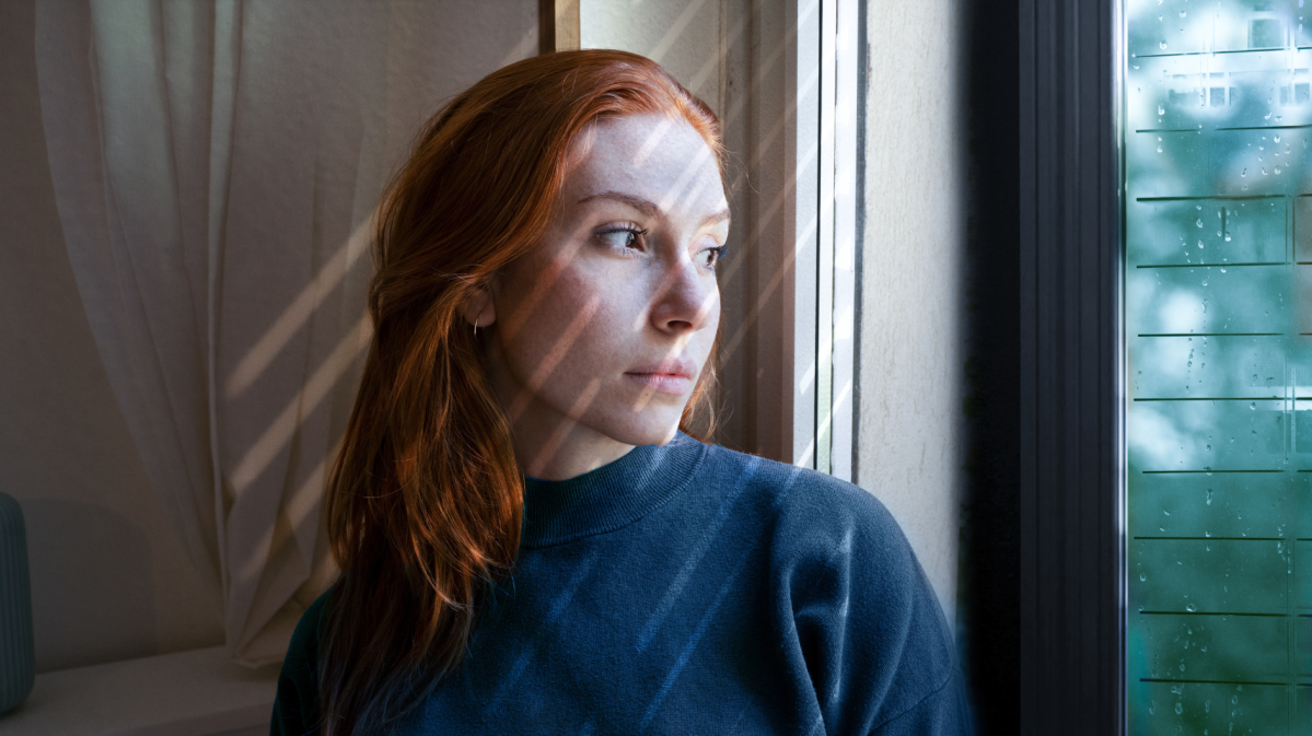 Rothaarige Frau, die nachdenklich aus dem Fenster schaut