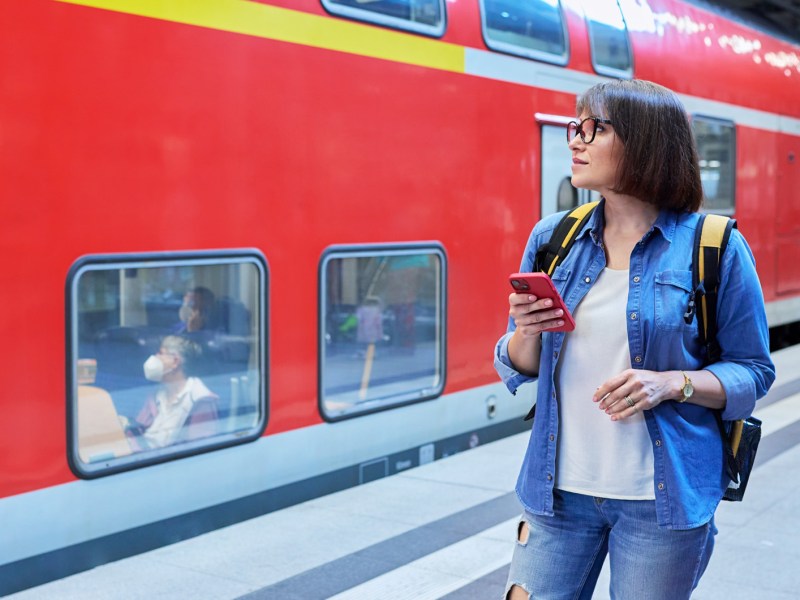 Frau steht mit dem Handy am Bahnsteig.