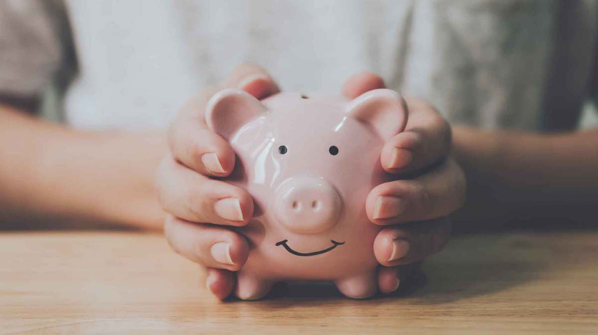 Junge Frau hält ein rosa Sparschwein in beiden Händen.