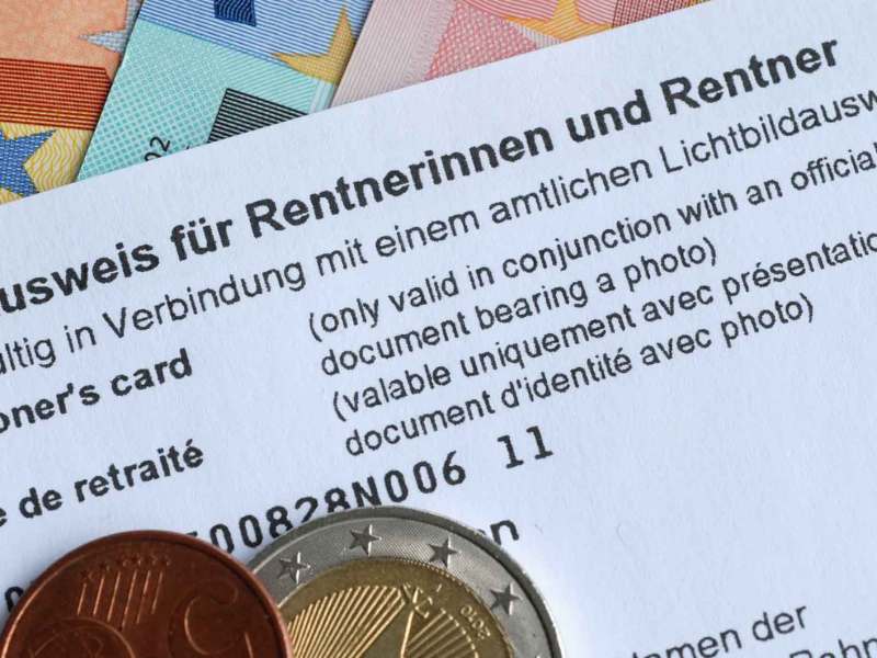Ein Rentenausweis liegt auf Geldscheinen. Darauf liegen Geldmünzen.