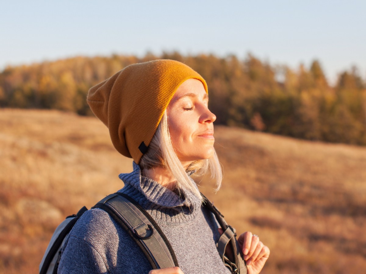 Frau in der Natur, die genussvoll in die Sonne blickt und einatmet