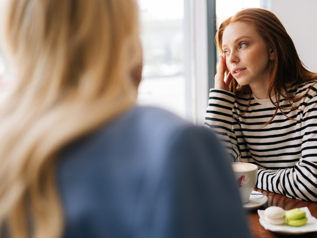 Zwei Frauen in einem Café, während die eine leicht verträumt zur Seite aus dem Fenster schaut