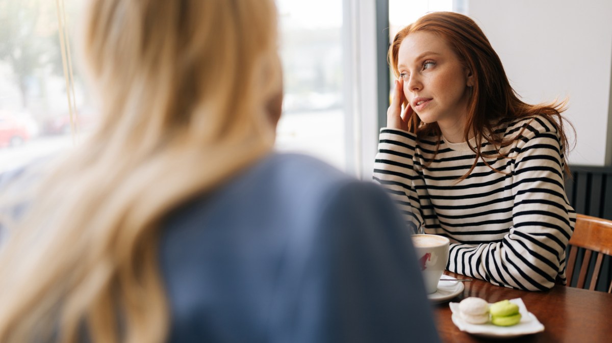 Zwei Frauen in einem Café, während die eine leicht verträumt zur Seite aus dem Fenster schaut