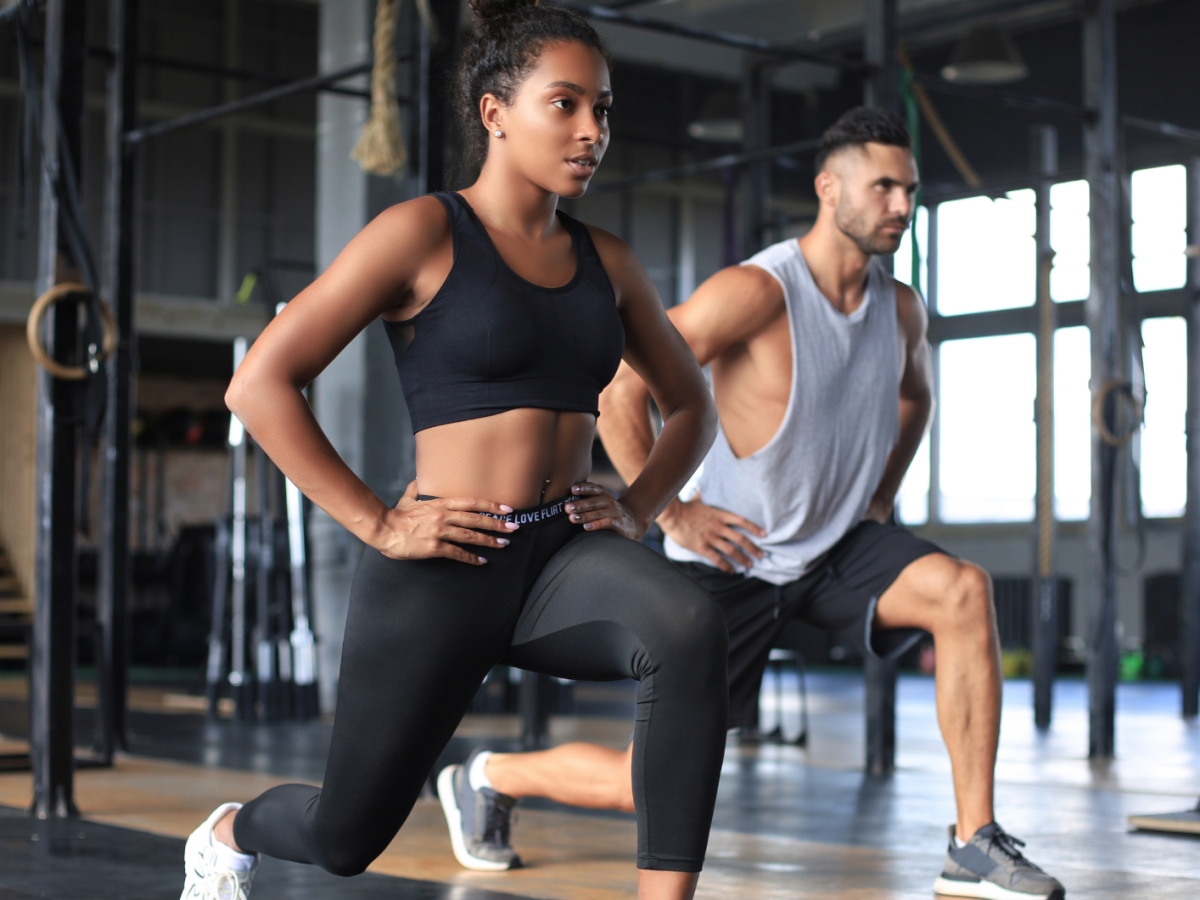 Frau und Mann im Fitnessstudio, die beide eine Kniebeuge machen und konzentriert nach vorne schauen