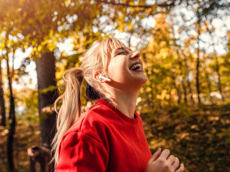 Frau im Wald, die lachend in Richtung Sonne schaut