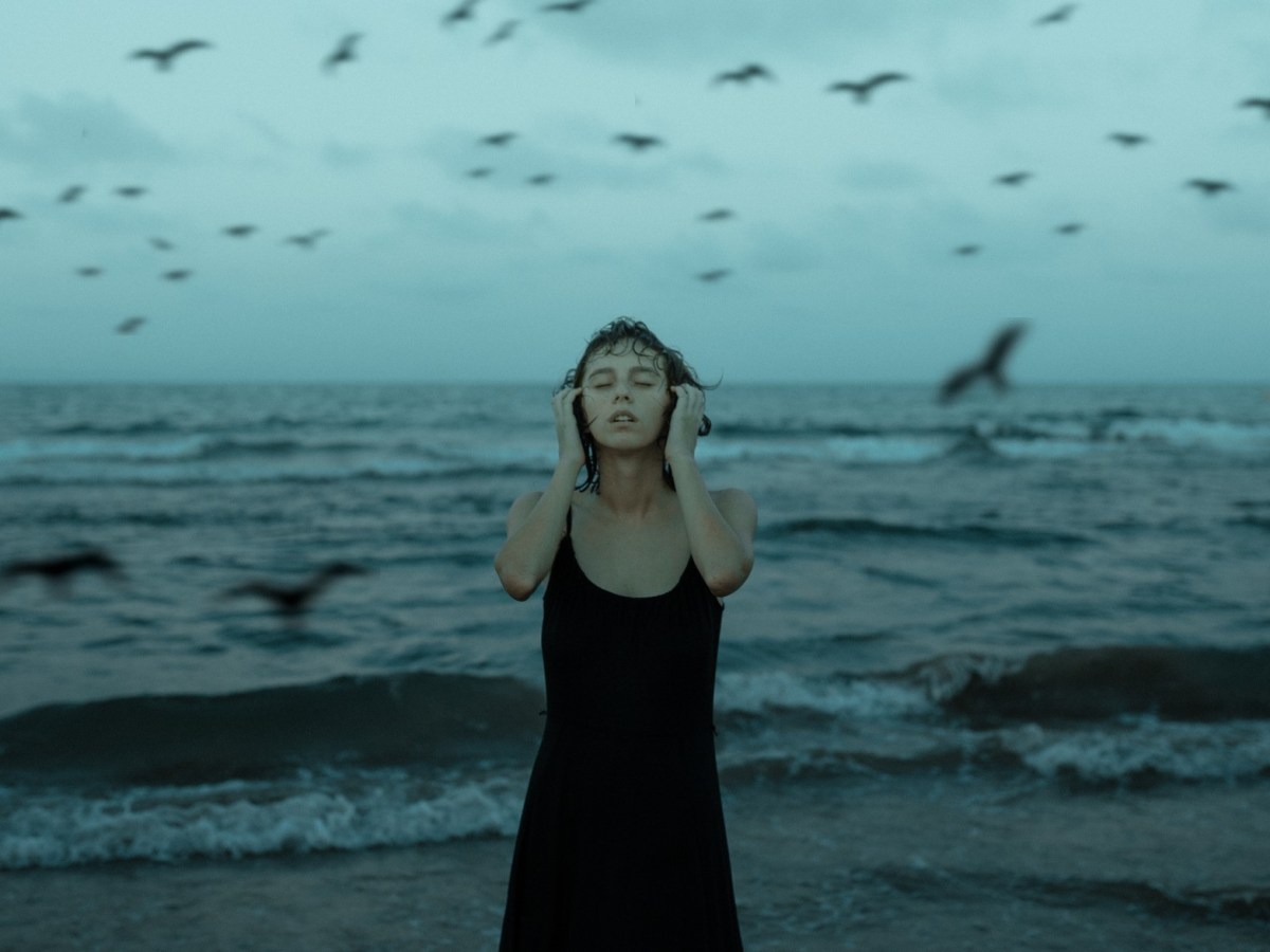 Frau mit geschlossenen Augen vor Meer mit Möwen, düstere Atmosphäre