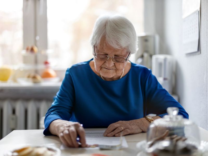 Rentnerin erledigt Papierkram und zählt Notgroschen am Tisch