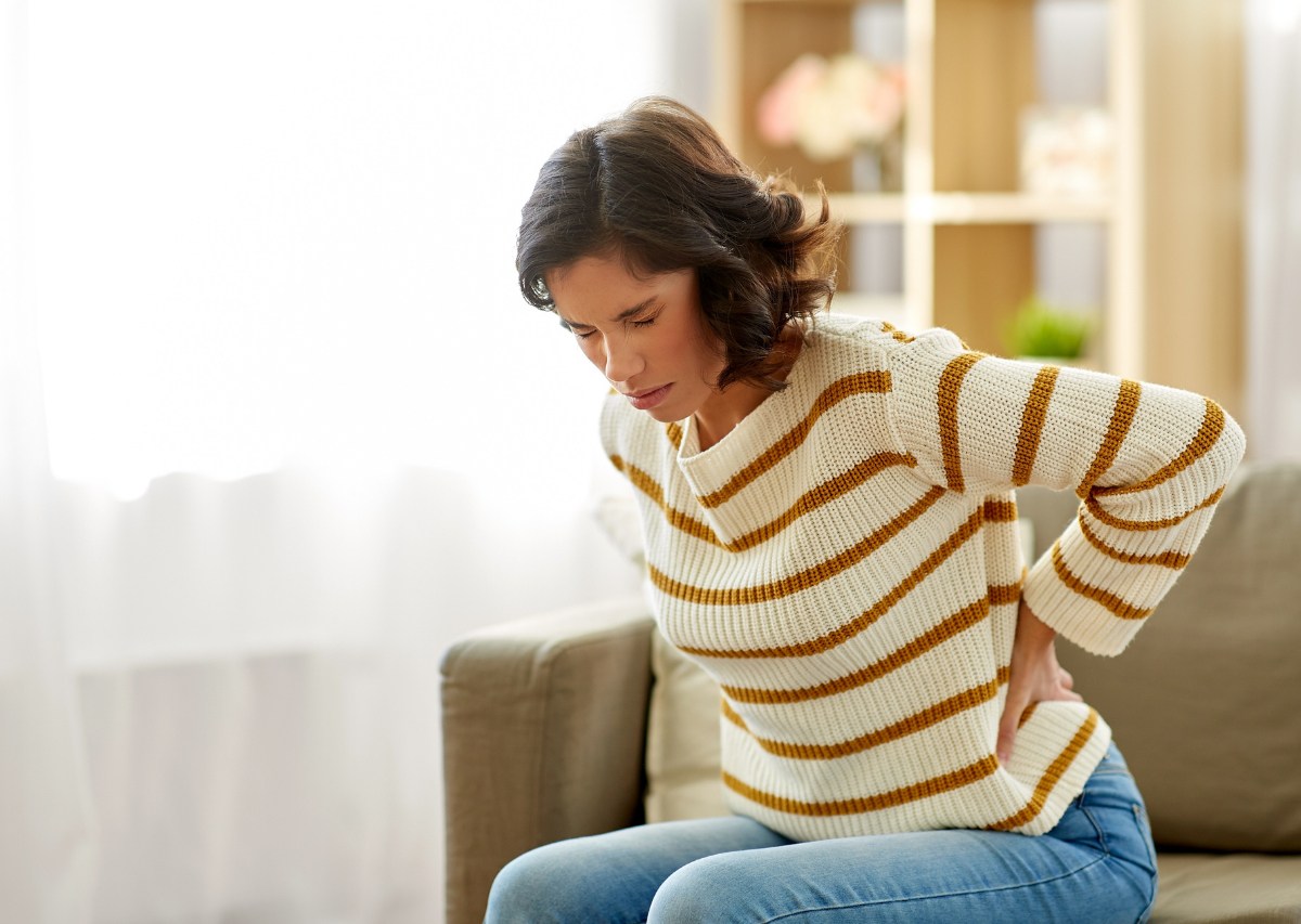 Eine Frau mit Ischiasschmerzen hält sich den Rücken.