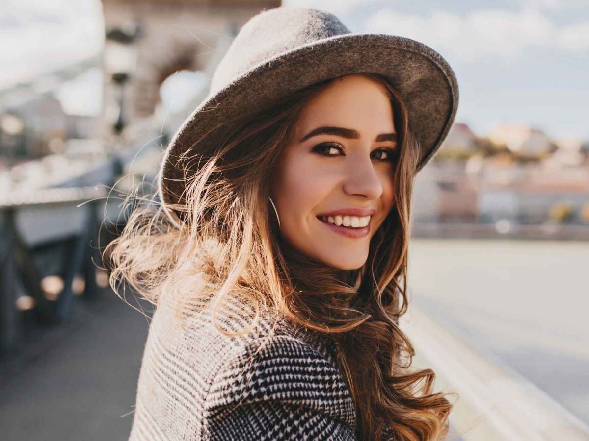 Frau auf einer Br&uuml;cke mit Hut lacht.