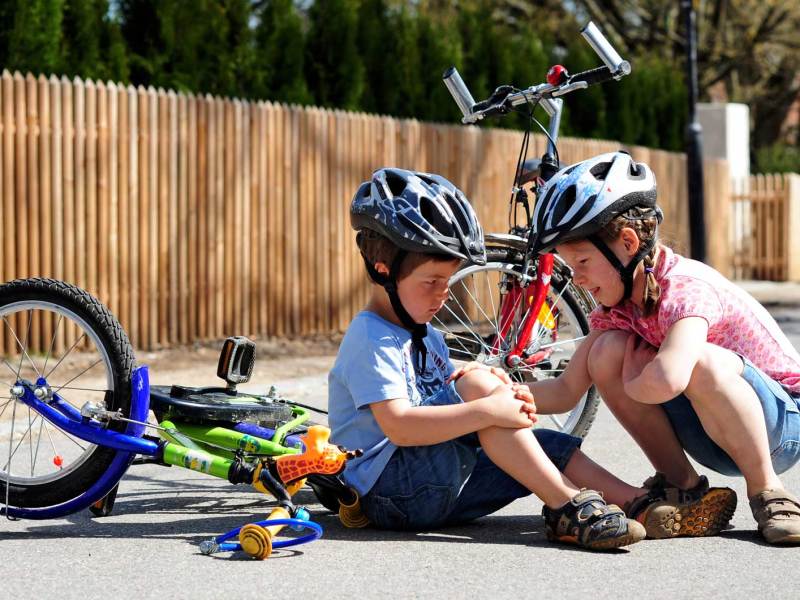 Gro&szlig;e Schwester hilft dem kleinen Bruder, der vom Fahrrad gefallen ist und sich wehgetan hat.