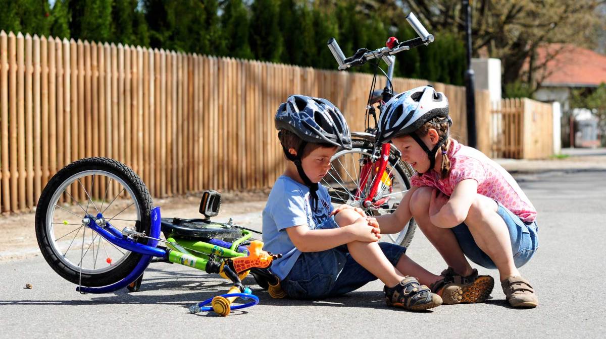 Große Schwester hilft dem kleinen Bruder, der vom Fahrrad gefallen ist und sich wehgetan hat.
