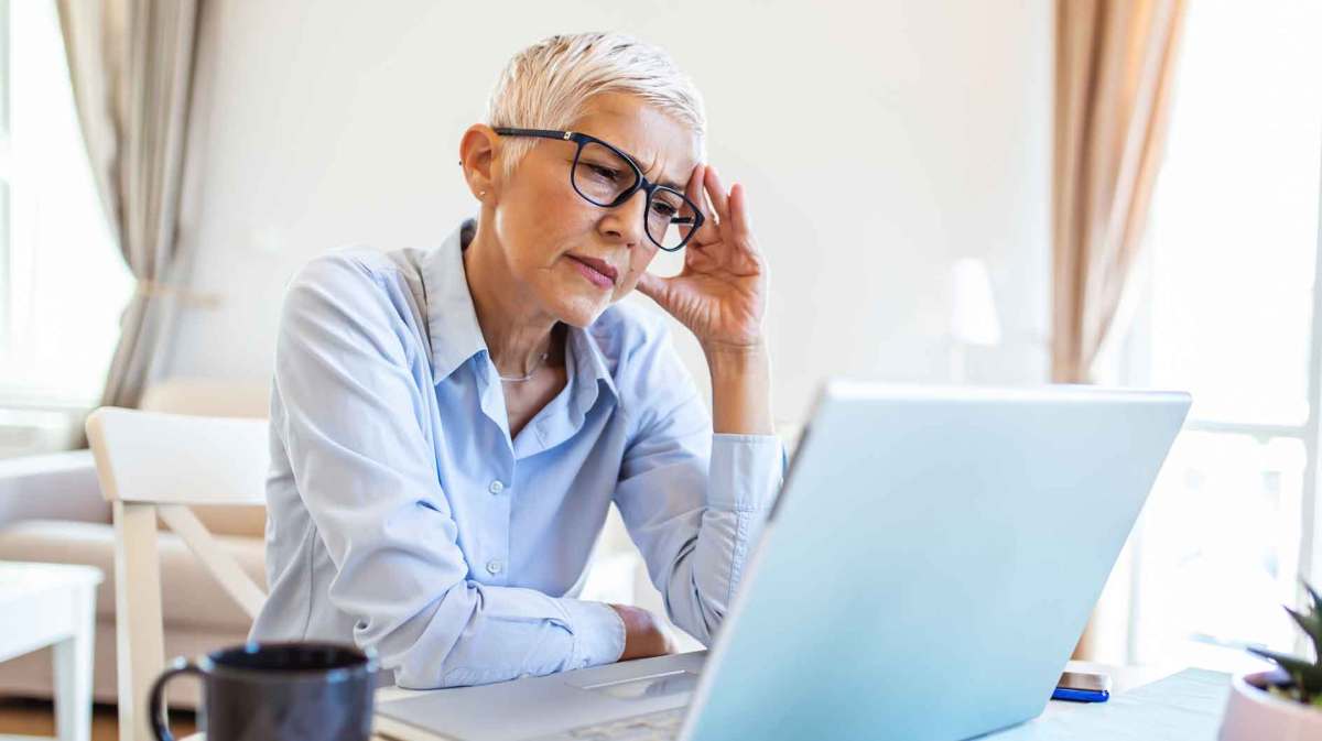 Ältere Frau mit kurzen weißen Haaren sitzt nachdenklich vor ihrem Laptop.