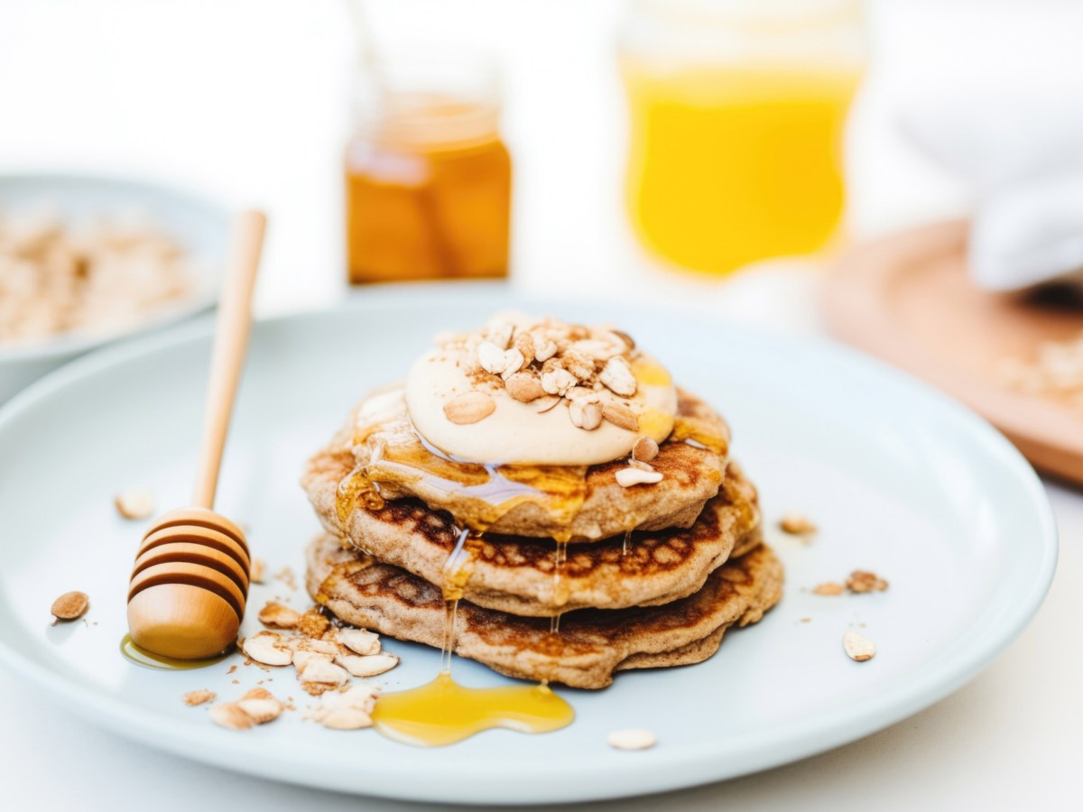 Haferflocken Pancakes auf einem weißen Teller mit Honig und Joghurt obendrauf.