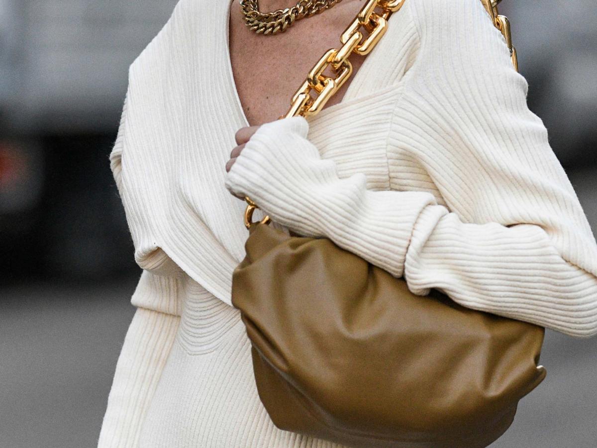 Frau mit weißem Pullover und beiger Lederhandtasche.