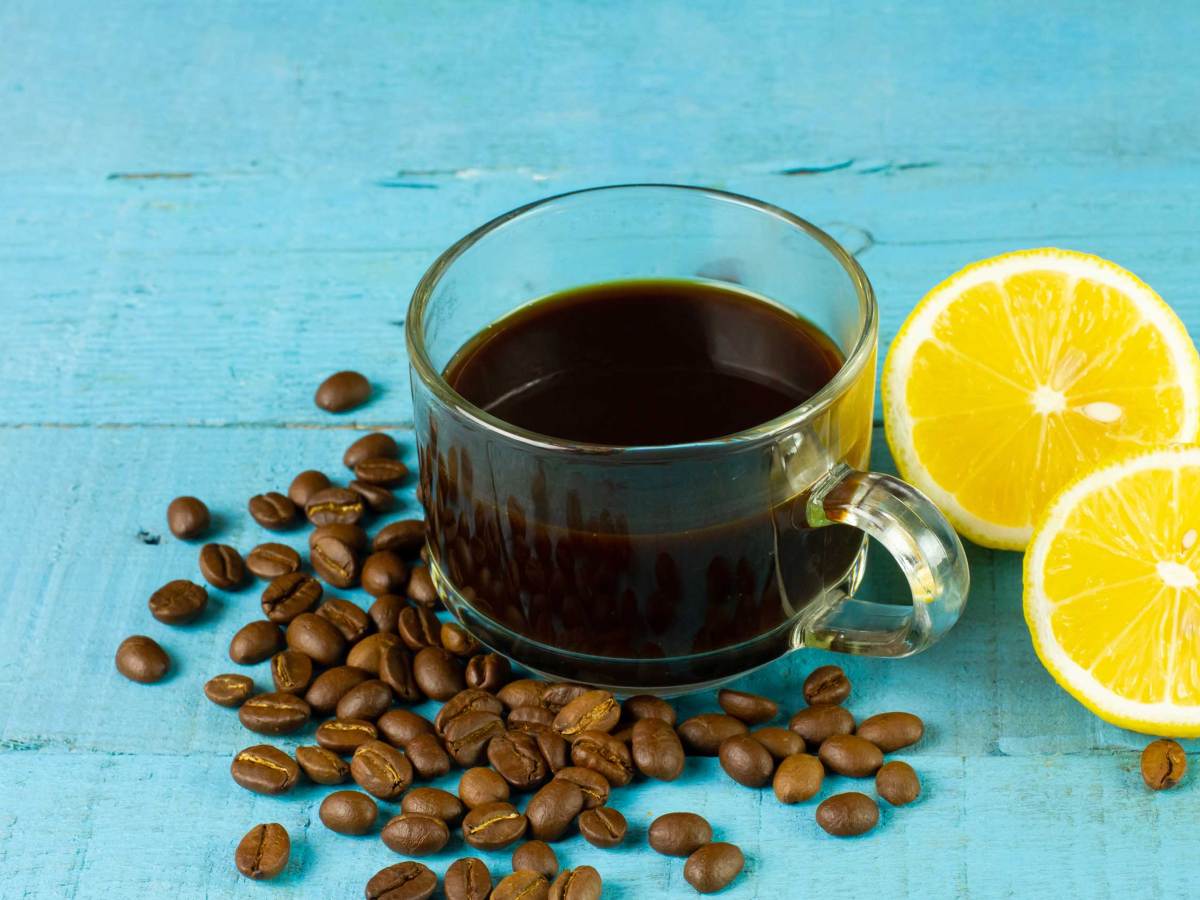 Schwarzer Kaffee in transparentem Glas mit frischer Zitrone und Kaffeebohne auf blauem Holzhintergrund. Espresso Romano