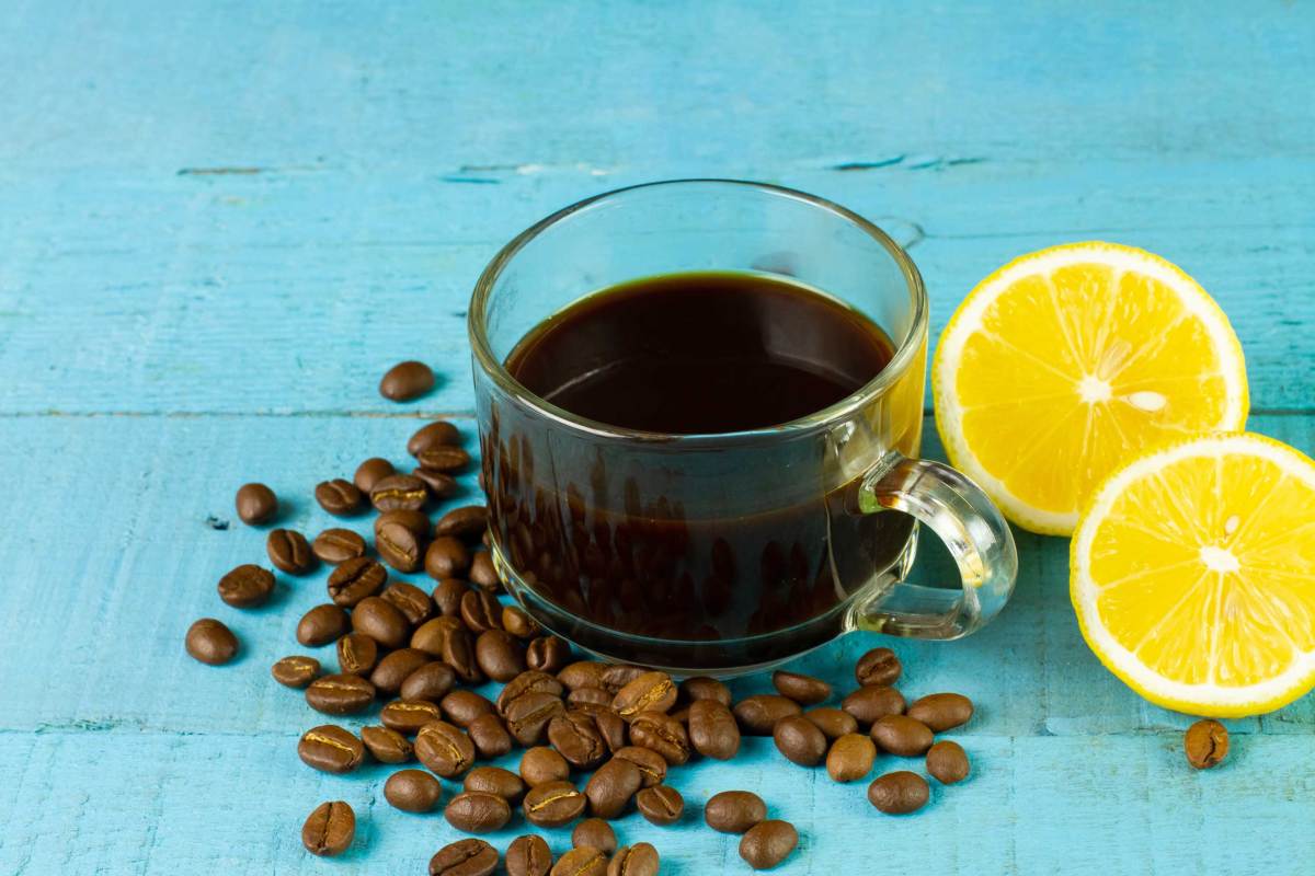 Schwarzer Kaffee in transparentem Glas mit frischer Zitrone und Kaffeebohne auf blauem Holzhintergrund. Espresso Romano