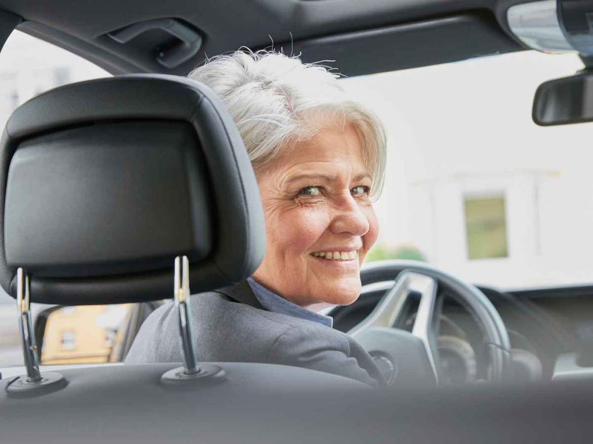 Ältere Frau fährt Auto und blickt nach hinten.