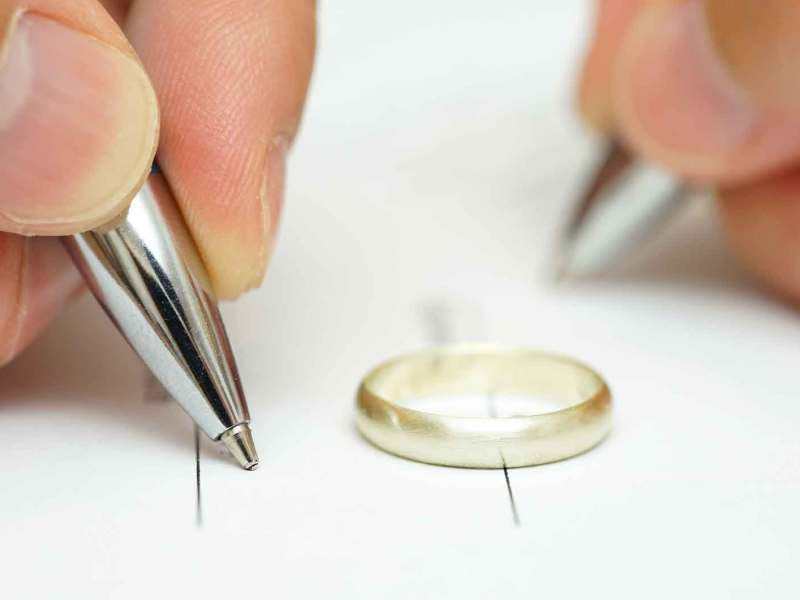 Mann und Frau unterschreiben einen Ehevertrag. In der Mitte liegt ein Ehering.