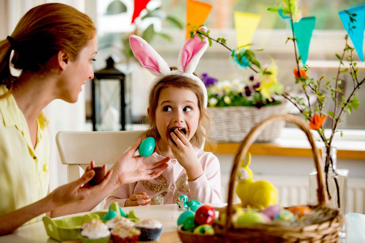 Mädchen und Mutter sitzen zu Ostern am Küchentisch und genießen Schokoladeneier.