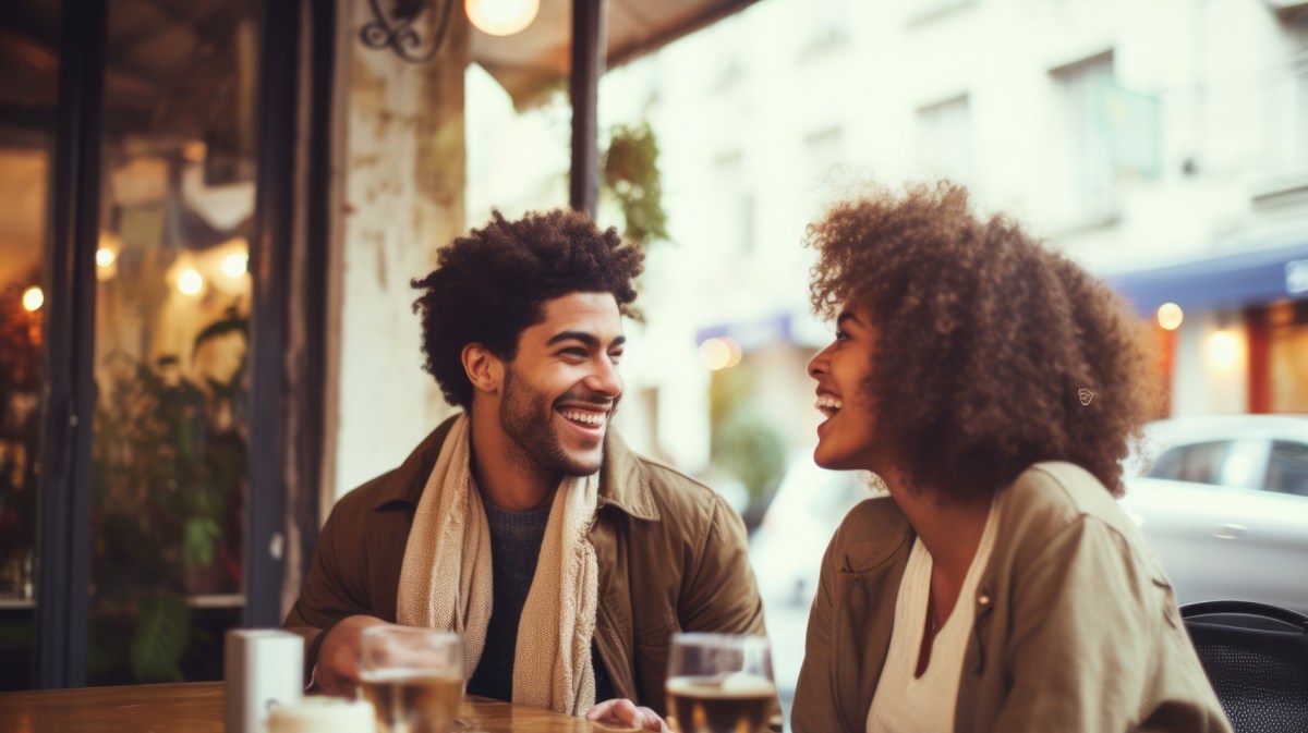 Frau und Mann in einem Café, die sich anlächeln und ein Getränk auf dem Tisch vor sich haben