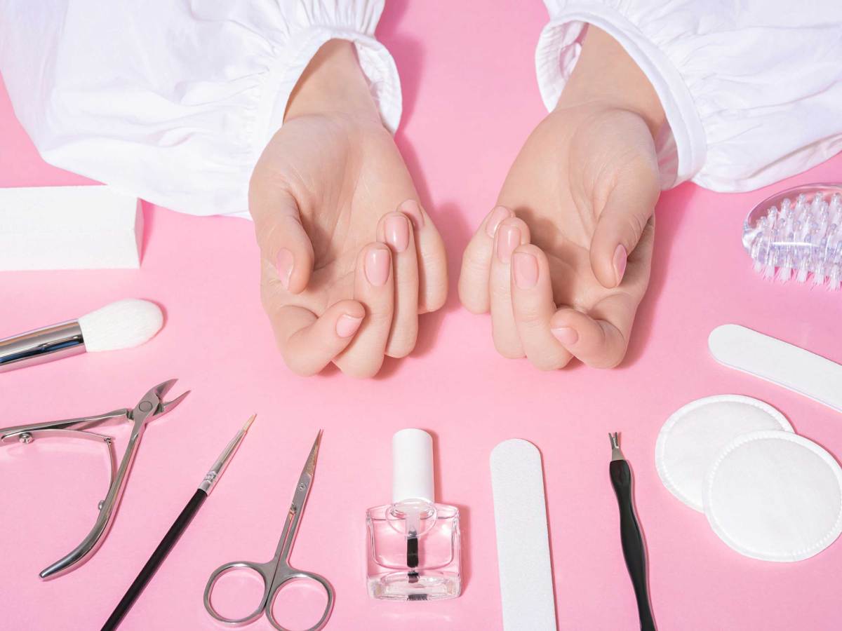 Nagelstudio Nahaufnahme von weiblichen gepflegten Händen und frisch manikürten Fingernägeln mit rosa Hintergrund. Schönheit und Pflege-Industrie-Konzept mit Maniküre-Tools, wie Schere, Zange und Pinzette.