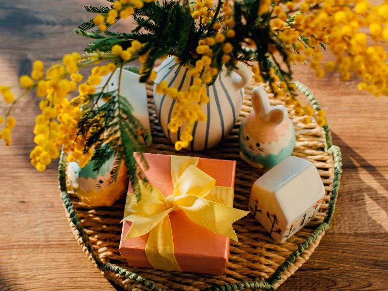 Geschenk, das auf einem Osterkorb steht, neben einem Porzellanhasen und einem kleinen Blumenstrauß.