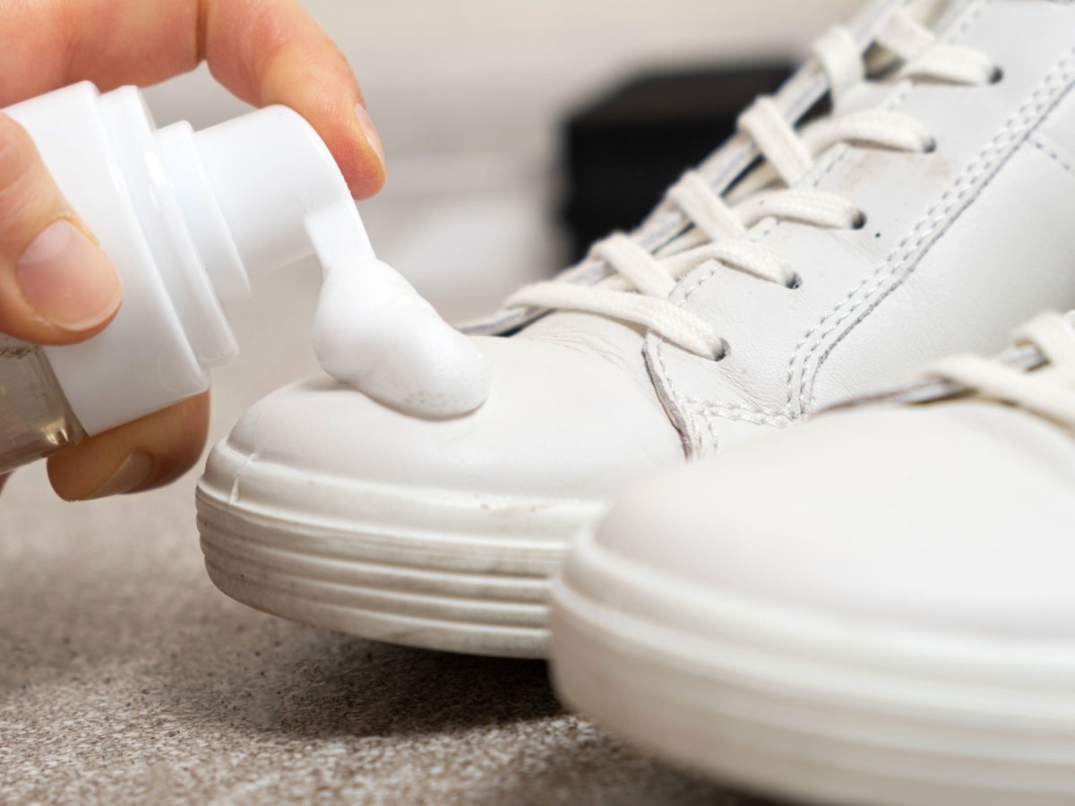 Hände geben Rasierschaum auf weiße Sneaker, um sie zu reinigen