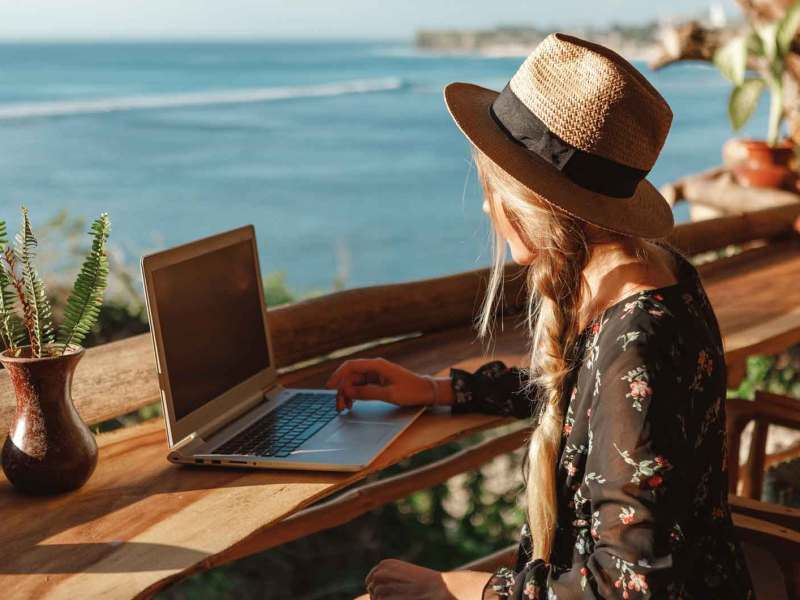 Frau sitzt vor Laptop am Strand.