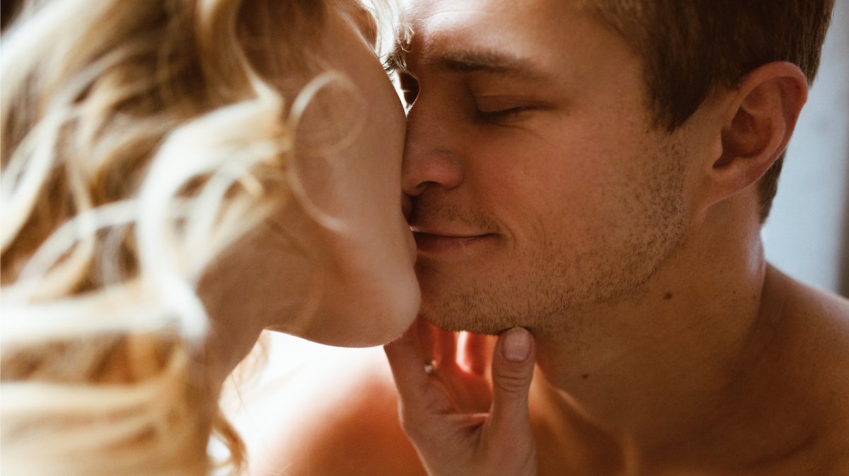 Ein junges Paar in Nahaufnahme berührt sich zärtlich, die blonde Frau hält das Kinn des lächelnden Mannes.