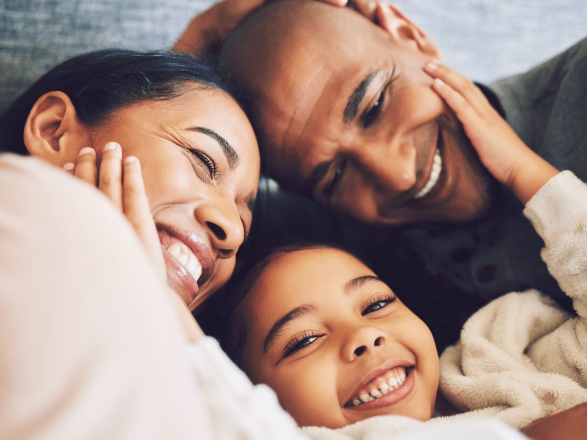 Familie, bestehend aus einer Mutter, einem Vater, einem Kind, die sich anl&auml;chelt und sich umarmt.