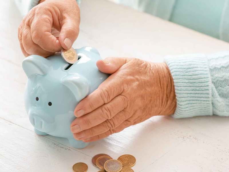 Frau wirft M&uuml;nzen in ein blaues Sparschwein.