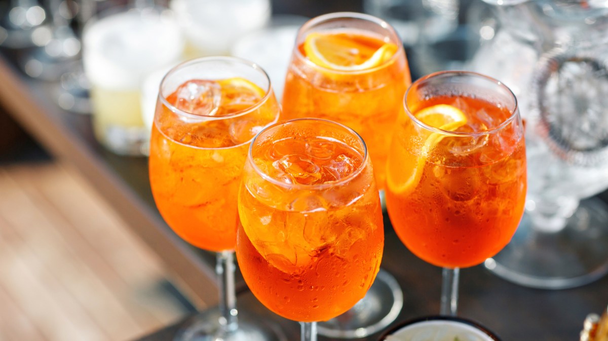 Vier Gläser mit Aperol Spritz auf einem Tisch.