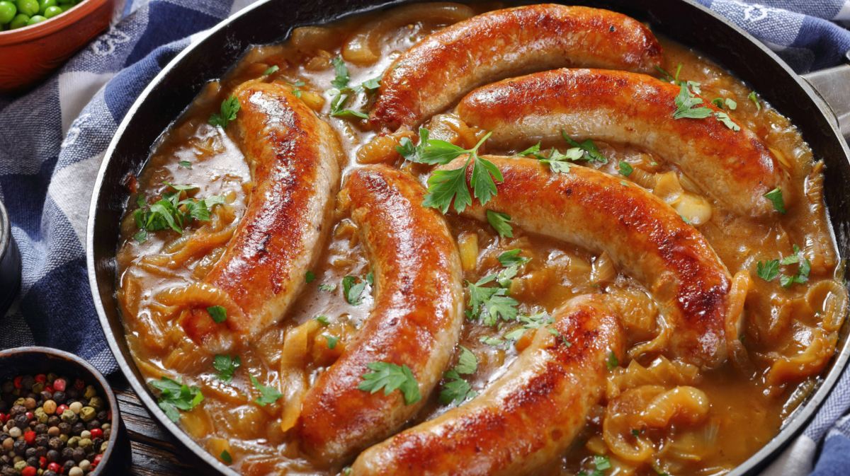 Bratwürste in Pfanne mit dunkler Soße.