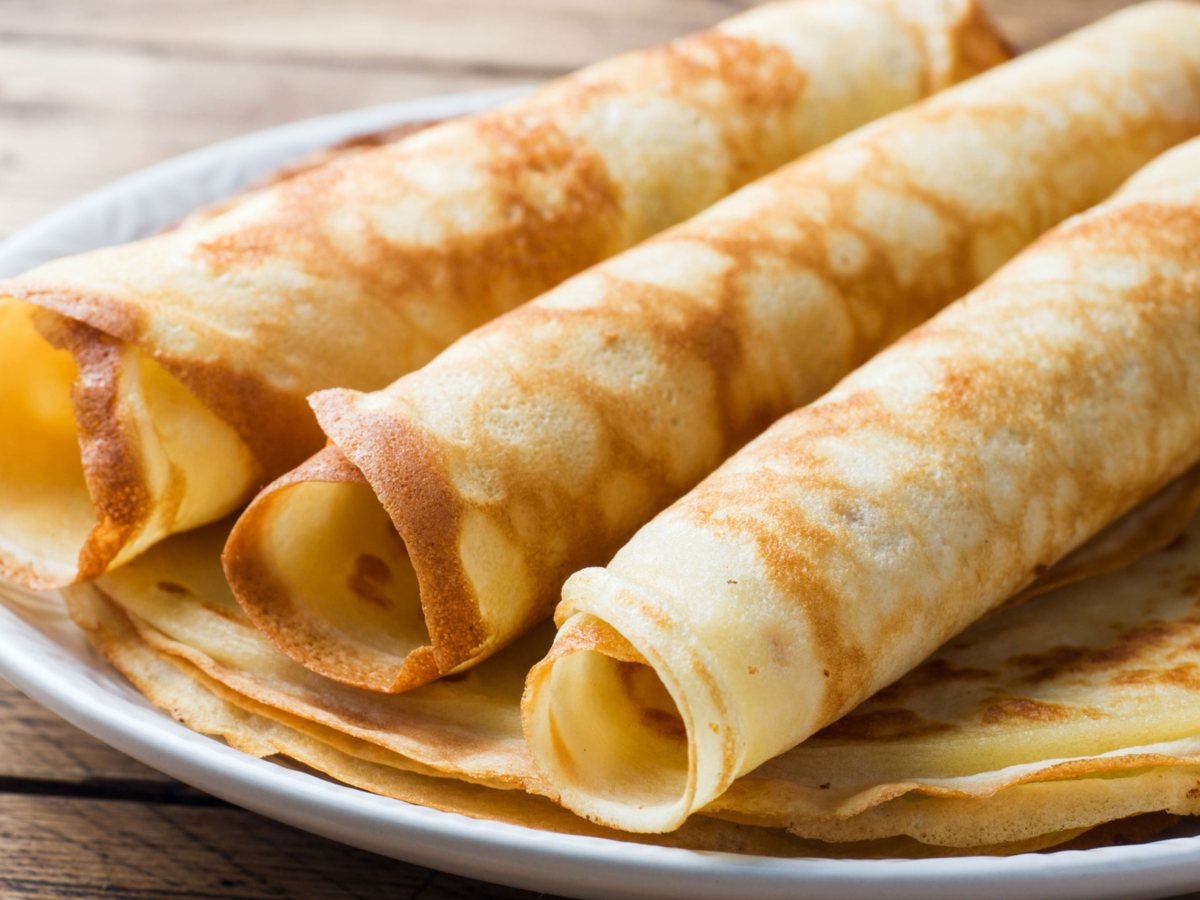 Dünne Crepe-Pfannkuchen auf einem Teller gestapelt, die obersten sind gerollt.