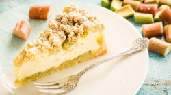 K&auml;sekuchen mit Streuseln und Rhabarber auf wei&szlig;em Teller.