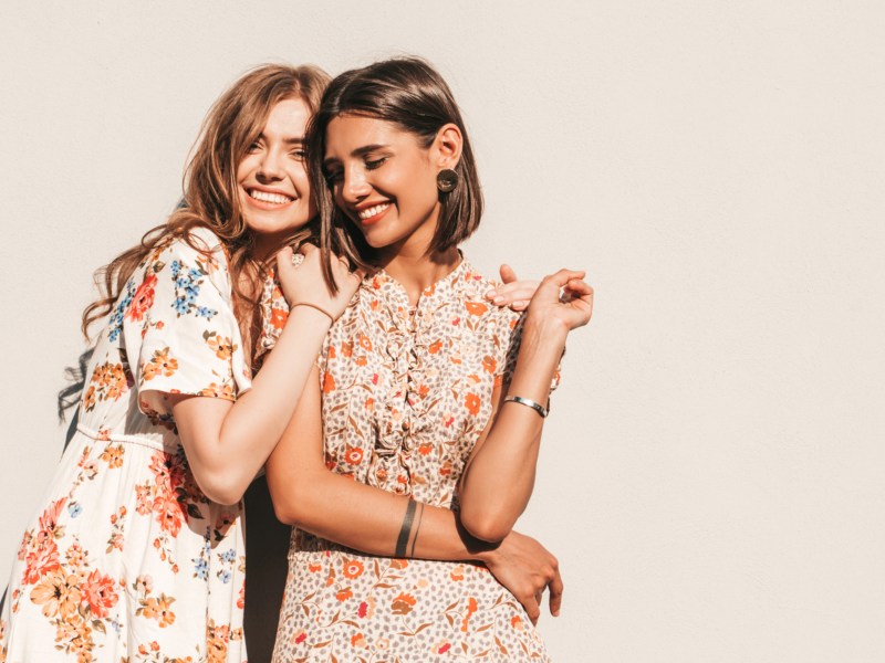 Zwei Freundinnen lächeln und lehnen sich an einander.