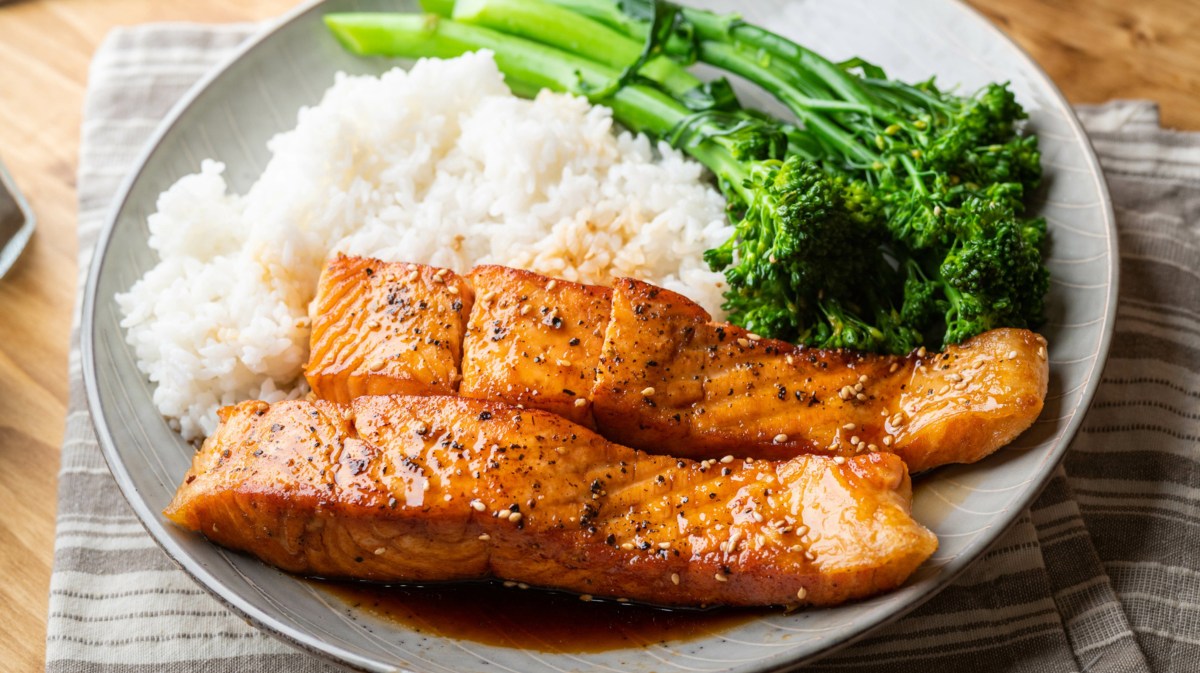 Teriyaki-Lachs mit weißem Reis und Brokkolini auf beigem Teller.