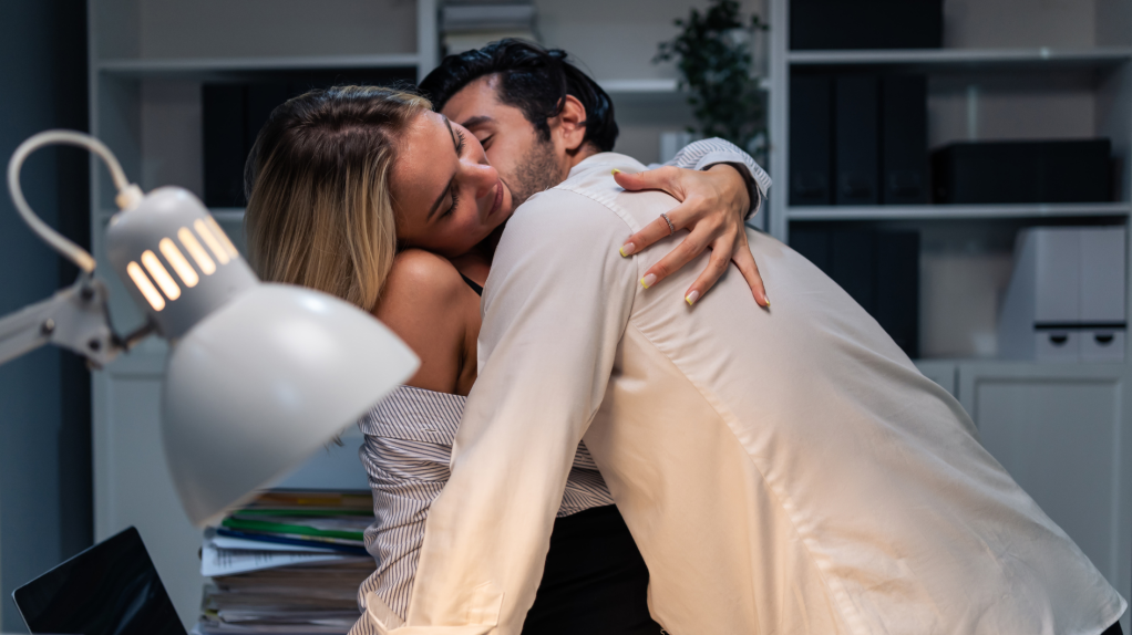 Pärchen, dass sich auf einem Schreibtisch leidenschaftlich auszieht.