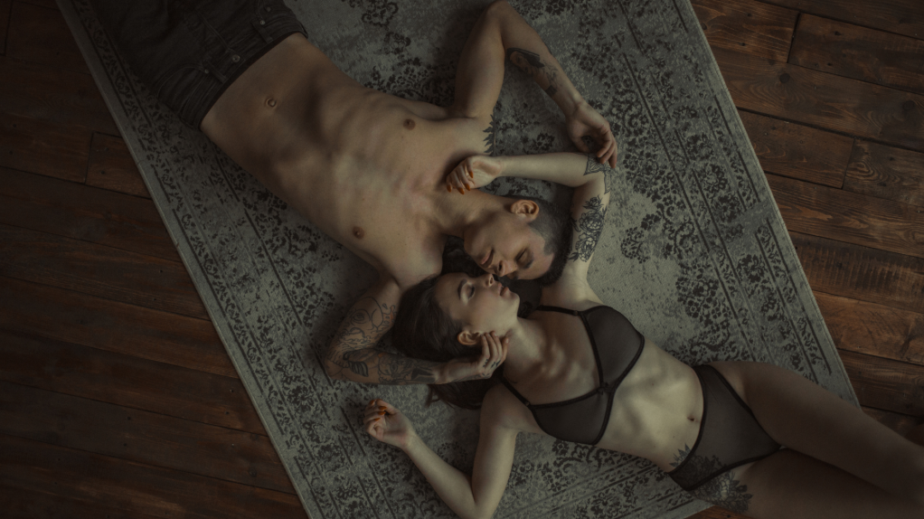 Ein Mann, der oberkörperfrei auf einem Teppich mit einer Frau im BH liegt