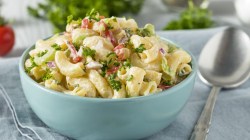 Nudelsalat in einer hellblauen Sch&uuml;ssel mit Petersilie und Speck.